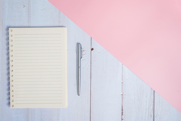 Imagen de la vista superior del cuaderno con bolígrafo en la mesa de madera con fondo rosa