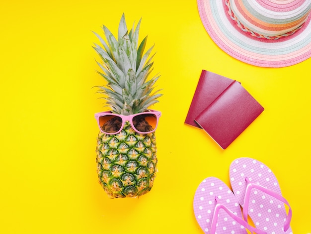 Imagen de vista superior de dos pasaportes, piña fresca con gafas de sol, zapatillas de playa y sombrero sobre un fondo amarillo.