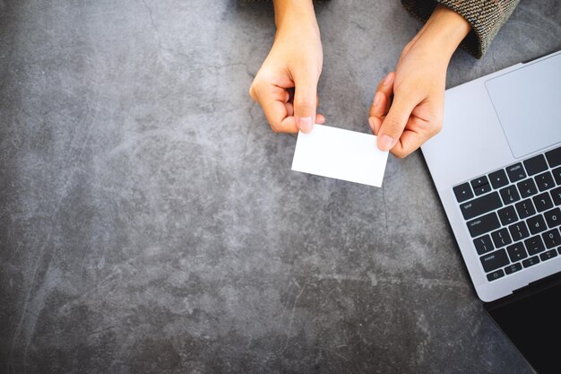 Imagen de la vista superior de una empresaria sosteniendo y dando tarjetas de visita en blanco mientras usa una computadora portátil en la oficina