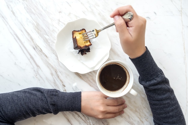 Imagen de la vista superior de una mano recogiendo el postre para comer con un tenedor y una taza de café en la mesa de café