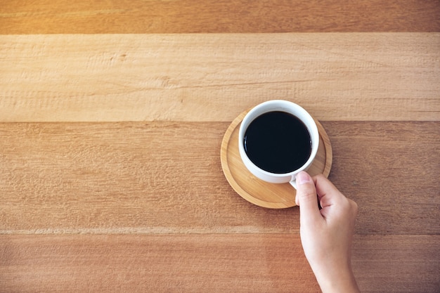 Imagen de la vista superior de la mano sosteniendo una taza blanca de café caliente para beber en la mesa de madera