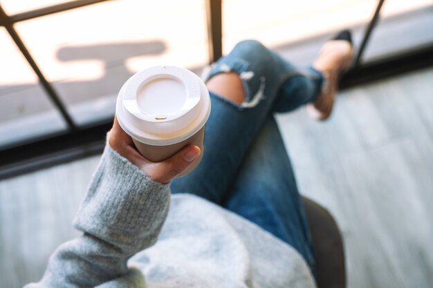 Imagen de la vista superior de una mujer sentada y sosteniendo una taza de papel de café caliente en la mañana