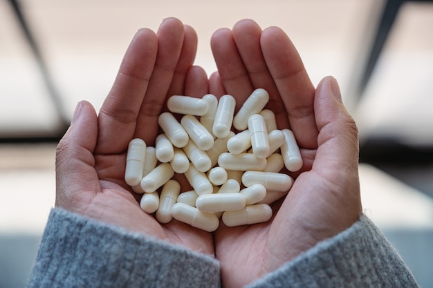 Imagen de la vista superior de una mujer sosteniendo cápsulas de medicina blanca en la mano