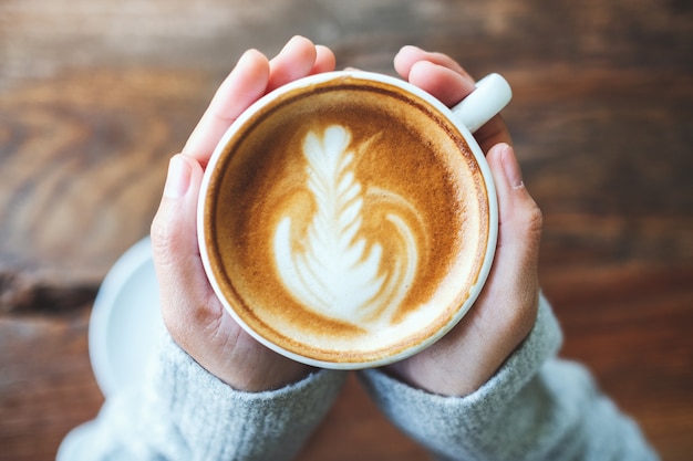 Imagen de la vista superior de una mujer sosteniendo una taza de café con leche caliente en la mesa de madera