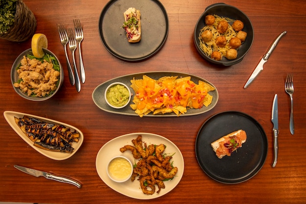 Imagen de vista superior de platos de comida internacional y mediterránea croquetas de jamón nachos con guacamole calamar rabas tostadas de salmón ahumado berenjena con jarabe de azúcar de caña