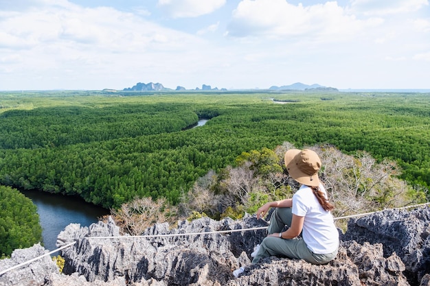 Imagen de la vista trasera de una hermosa joven asiática sentada en la cima de la montaña mientras viaja por el mirador del bosque de manglares