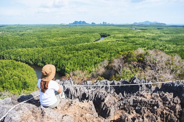 Imagen de la vista trasera de una hermosa joven asiática sentada en la cima de la montaña mientras viaja por el mirador del bosque de manglares