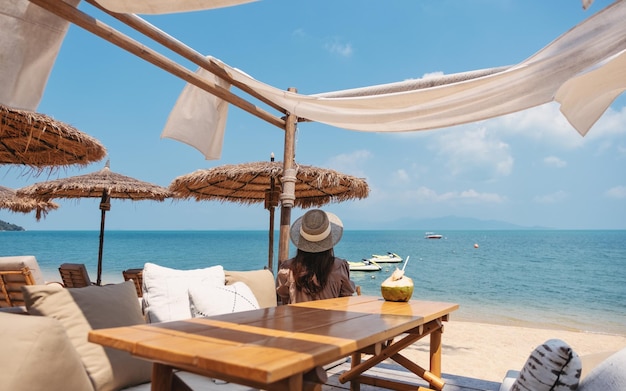 Imagen de la vista trasera de una mujer mirando un hermoso mar mientras se sienta en el café en la playa