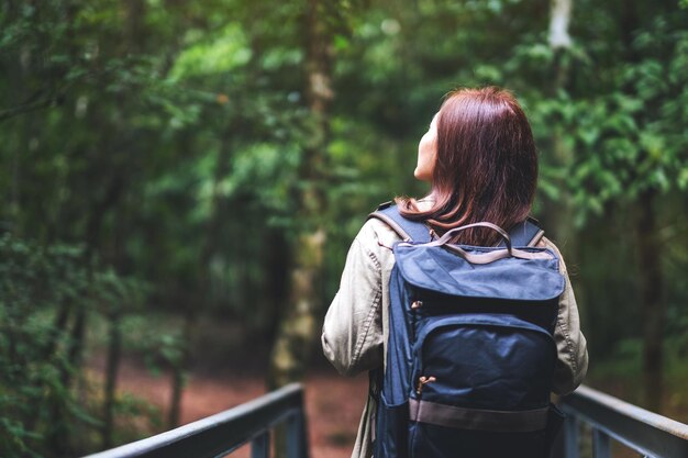 Imagen de vista trasera de una mujer viajera con mochila caminando hacia el bosque