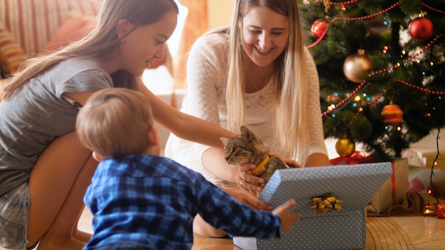 Imágenes de 4 k de familia feliz abre regalos y regalos de Navidad. Lindo gatito saliendo de la caja. Familia pasando un buen rato y divirtiéndose en las vacaciones y celebraciones de invierno.