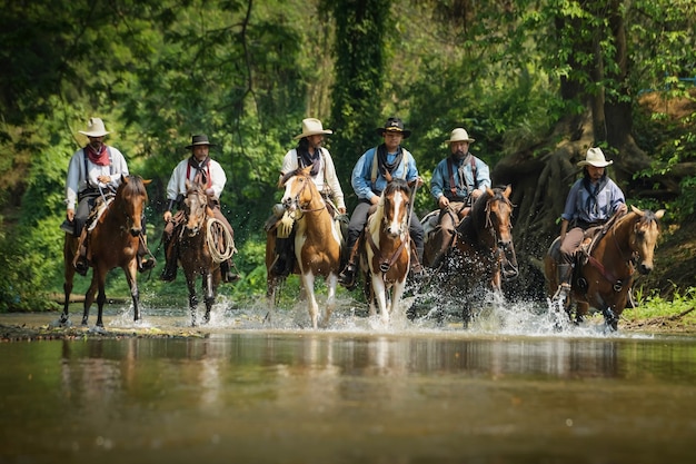 Imágenes de muchos hombres vestidos con ropa de vaquero, montando a caballo y cruzando el río