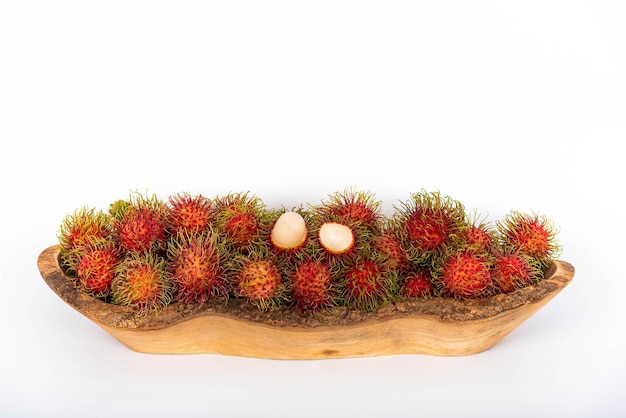 Las imágenes de objetos de muchos rambután frescos en un tazón de madera se alimentan de frutas y sabor dulce sobre fondo blanco.