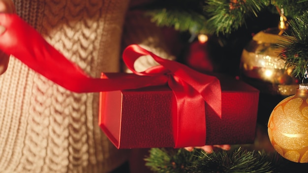 Imágenes de primer plano 4k de mujer joven tirando de la cinta roja y desenvolviendo la caja con regalo de Navidad