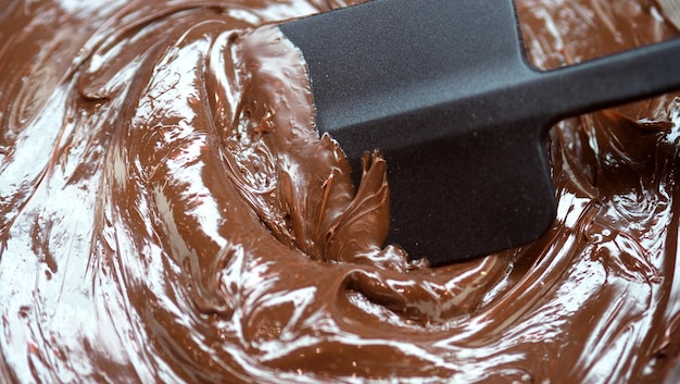 Imágenes de primer plano del ángulo de visión superior de la barra de chocolate y semillas de cacao con un tazón de leche crema marrón oscuro girando a mano para representar uno de los deliciosos dulces del mundo