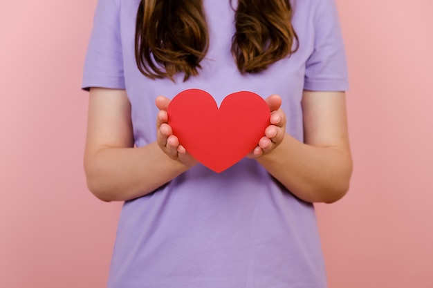 Imágenes recortadas de la joven bloguera sostiene en las manos un pequeño corazón rojo, aislado sobre fondo rosa de estudio. Como concepto de ternura de redes sociales de blogs de blogs. San Valentín internacional de mujeres