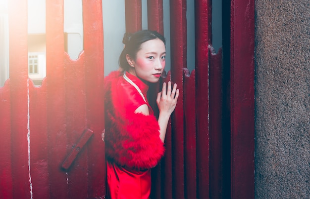 Imágenes de retratos de una niña china vestida con un vestido rojo de Cheongsam, de pie sobre una puerta de madera roja.