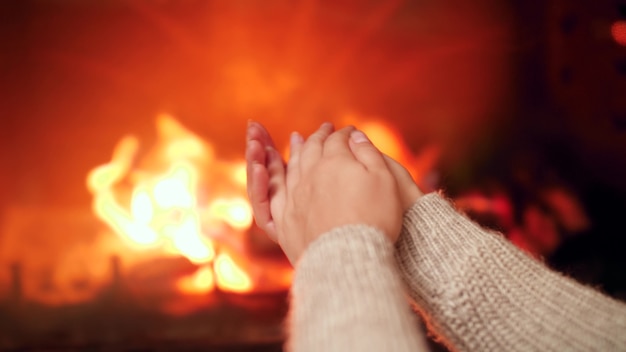 Imagens de 4K de close de uma jovem esfregando as mãos e aquecendo o dedo frio perto do fogo na lareira em casa