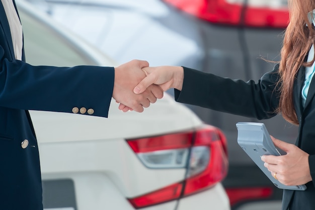 Imagens de clientes e vendedores asiáticos, de mãos dadas, felizes em comprar carros novos que fazem acordos de vendas com revendedores de automóveis.