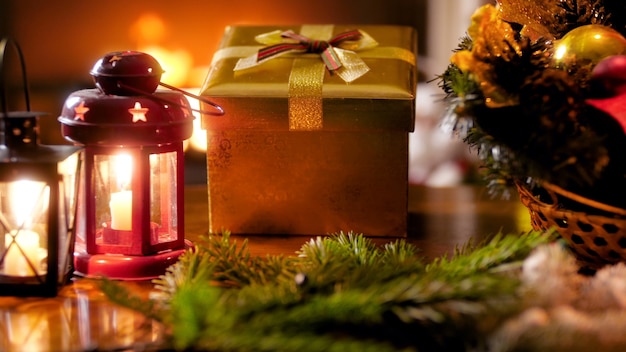 Imagens de closeup 4k de guirlanda de natal, lanterna de vela e presente de ano novo do papai noel na mesa de madeira contra a lareira a lenha. foto perfeita para celebrações e feriados de inverno