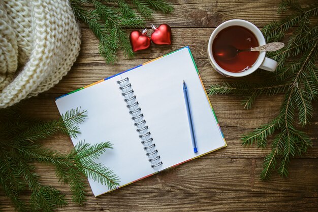 Imagens de Natal de inverno: bloco de notas com caneta, xícara de chá, ramos de abeto, corações de brinquedo e cachecol