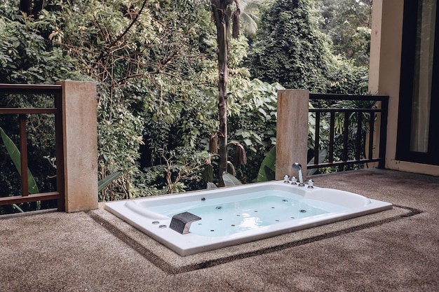 Imagens de um jacuzzi ao ar livre vazio branco luxo elegante com água. Relaxe na natureza no contexto das plantas. Férias caras no exterior em uma vila nos trópicos.