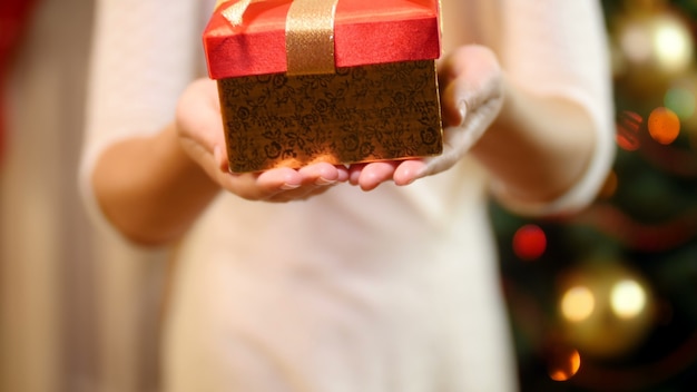 Imagens do close up de uma jovem mulher com um vestido segurando uma caixa de presente de Natal e mostrando-a na câmera. Família dando e recebendo presentes nas comemorações e feriados de inverno.