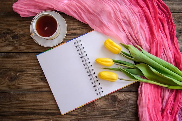 Imagens românticas com o bloco de notas, tulipas e uma xícara de chá em fundo de madeira