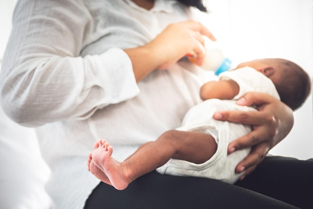 Imagens suaves desfocadas de mãe alimentando leite de mamadeira para bebê africano recém-nascido de pele negra