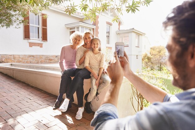 Foto imagine a família e a avó feliz, mãe e filho, sorrindo e pai tirando fotos de gerações ao ar livre suporte de celular e felicidade da mãe de criança e avó idosa no quintal de casa