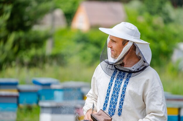 Imker in Arbeitsschutzkleidung. Nesselsucht Hintergrund im Bienenhaus. Arbeitet an den Bienenständen im Frühjahr.