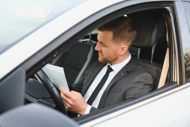 Immer in Eile Hübscher junger Mann im vollen Anzug, der beim Autofahren lächelt