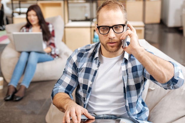 Immer in Kontakt. Kluger hübscher sicherer Mann, der im Büro sitzt und ein Telefongespräch führt, während Arbeitsprobleme besprochen werden