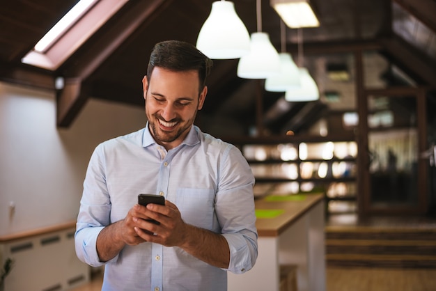 Immer in Kontakt. Netter hübscher junger Mann, der sein intelligentes Telefon im Haus verwendet.