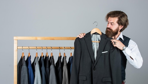 Immer verfügbarer Schneider in seiner Werkstatt Schöner bärtiger Modemann im Kostümanzug Mann im maßgeschneiderten Anzug, der teure maßgeschneiderte Smokings präsentiert Mannkleidung in der Boutique Mann mit Anzug