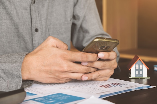 Immobilienagentur, die mit intelligentem Telefon und Dokument auf Holztisch im Büro arbeitet