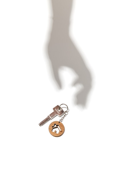 Immobilienkonzeptschlüssel mit hausförmigem Schlüsselbund mit Handschatten auf weißem Hintergrund