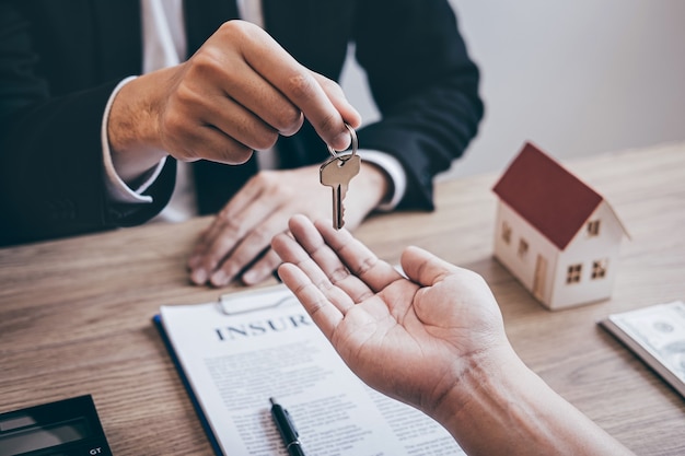 Foto immobilienmakler, der dem kunden hausschlüssel nach unterzeichnung des immobilienvertrags mit genehmigtem hypothekenantragsformular über hypothekendarlehensangebot und hausversicherung übergibt.
