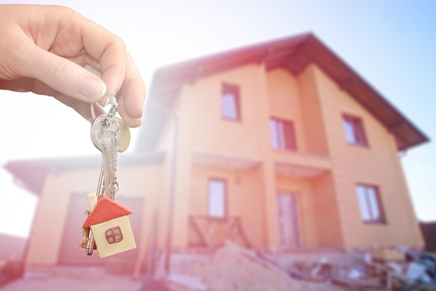 Immobilienmakler, der einen Hausschlüssel übergibt Schlüssel mit einer Schlüsselkette in der Form des Hauses auf neuem Haupthintergrund Hypothekenkonzept