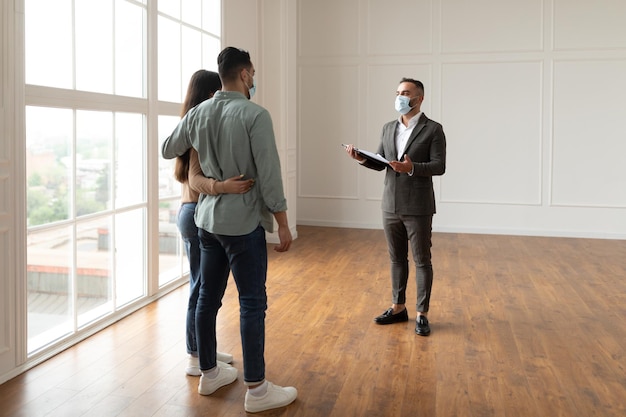 Immobilienmakler in Gesichtsmaske, der Käufern neue Wohnung zeigt