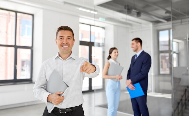 Immobilienmakler mit einem Ordner, der auf Sie im Büro zeigt