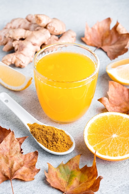 Immunstärkendes Getränk mit Zitrusfrüchten, Ingwer, Kurkuma. Trinken oder Smoothie mit gelben Herbstblättern für die Herbst- oder Virussaison auf neutralem beigem Hintergrund, Stillleben