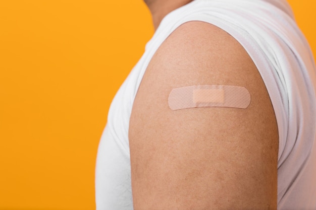 ImpfkampagneNahaufnahme Junger indischer Mann, der Coronavirus-Impfstoff erhält, immun und Arm mit Pflaster auf isoliertem gelbem Hintergrund zeigt