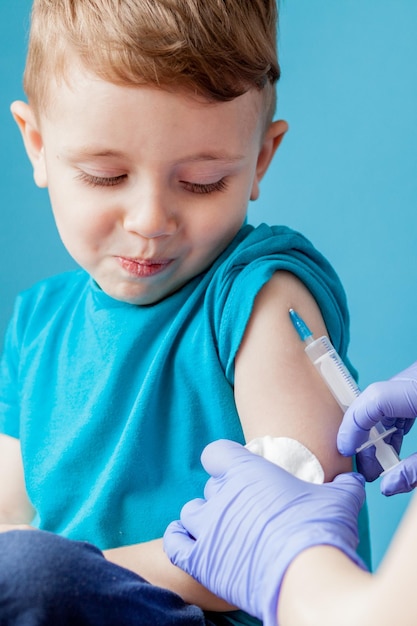 Impfkonzept Ärztin impft niedlichen kleinen Jungen auf blauem Hintergrund, Nahaufnahme