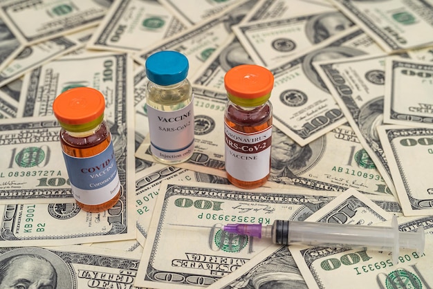 Impfstoff in Flaschen mit Spritzenrechner und auf dem Tisch liegenden Dollarnoten Das Konzept der bezahlten Impfung
