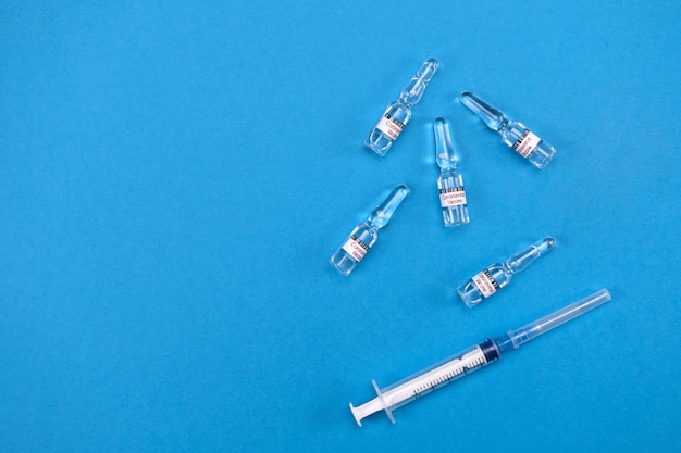 Foto impfstoff zur behandlung von covid-19-coronavirus mit spritze auf blauem hintergrund mit platz für text