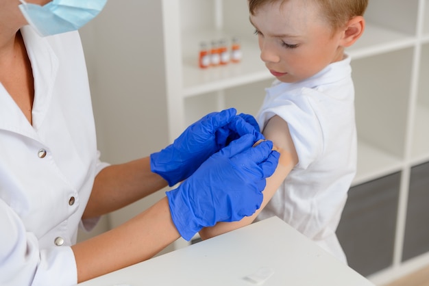 Impfung des Kindes. Arzt klebt ein Pflaster an die Injektionsstelle, Nahaufnahme