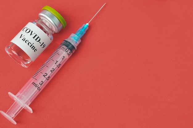 Impfung mit Spritze und Covid19-Flasche auf rotem Hintergrund