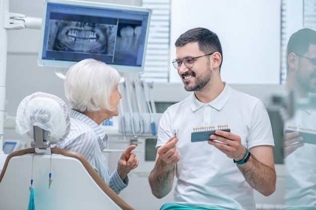 Implantes dentales. Varón joven dentista eligiendo implantes dentales con su paciente