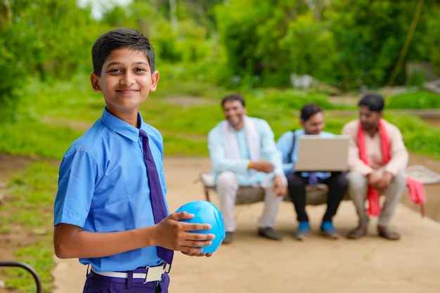 importancia del concepto de ahorro: Niño indio inteligente de pie y sosteniendo la hucha en la mano en casa.