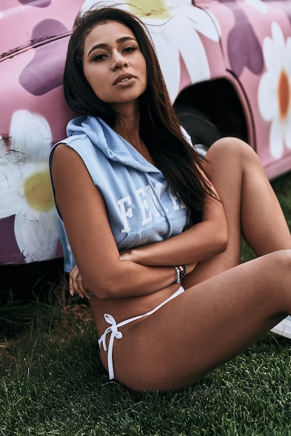 Imposible resistirse a su belleza. Atractiva mujer joven mirando a la cámara y manteniendo los brazos cruzados mientras está sentado al aire libre